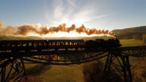 photo of a steam locomotive and train crossing a large trestle bridge