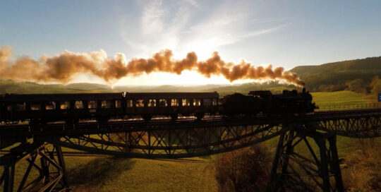 photo of a steam locomotive and train crossing a large trestle bridge