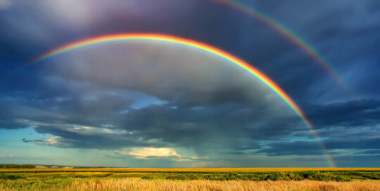Rainbow over stormy sky. Rural landscape with rainbow over dark stormy sky in a countryside at summer day.