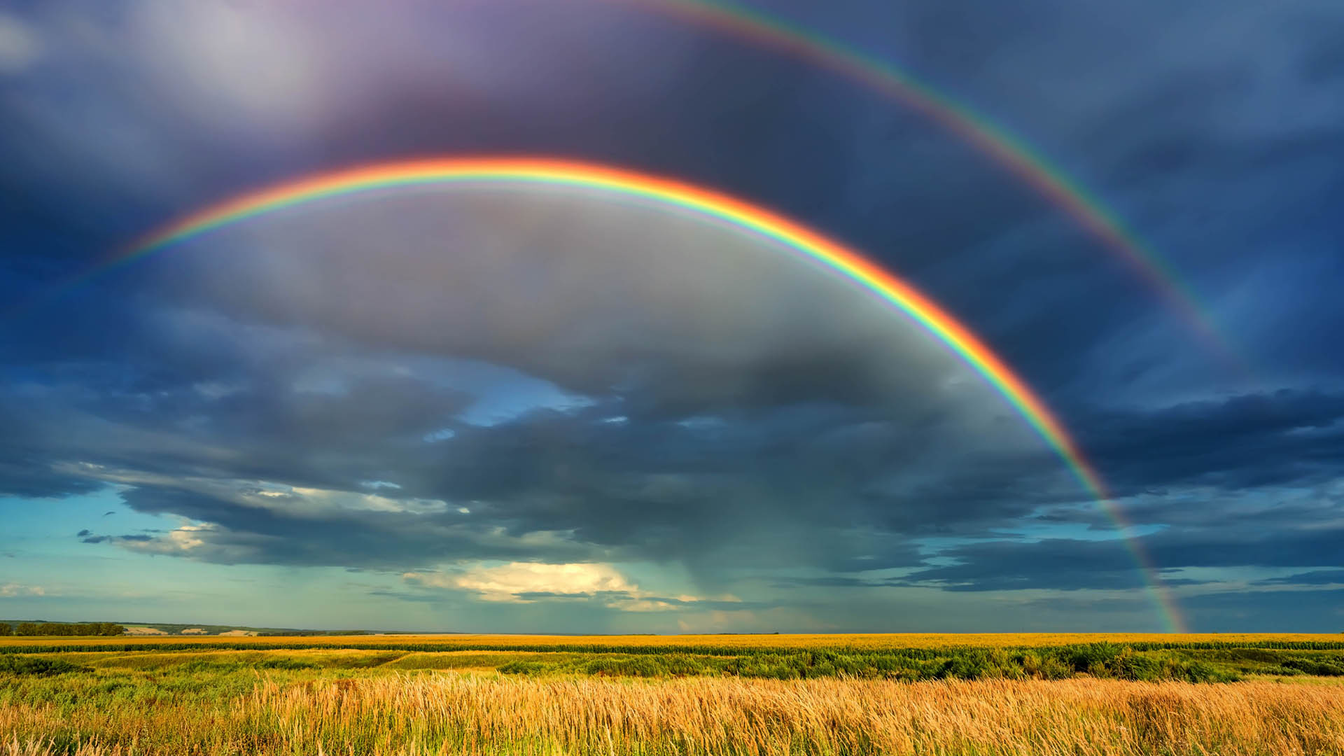 Rainbow over stormy sky. Rural landscape with rainbow over dark stormy sky in a countryside at summer day.